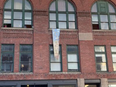 a colorful banner that says "COURAGE"  hangs from the large arched windows of the Bangor Arts Exchange, a beautiful old brick building in downtown Bangor, during the 2022 First Light Summit.